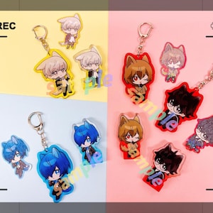 May include: Keyrings featuring anime-style characters with animal ears. The keyrings have a clear acrylic design with gold-coloured metal key rings. The characters have various hair colours and outfits, set against yellow and pink backgrounds.