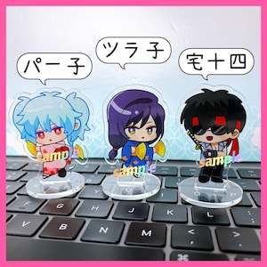 Könnte beinhalten: Drei Anime-Charakterfiguren aus Acryl mit japanischem Text in Sprechblasen. Jede Figur ist ein Charakter im Chibi-Stil mit einzigartigen Haaren und Kleidung. Die Figuren stehen auf transparenten Sockeln, auf denen das Wort "sample" aufgedruckt ist.