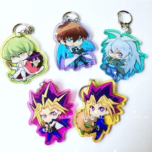 Puede incluir: Cinco llaveros de personajes de anime coloridos con fondo negro. Los llaveros presentan personajes de la serie de anime Yu-Gi-Oh! Los personajes están todos en estilo chibi y llevan sus atuendos característicos. Los llaveros están hechos de acrílico transparente y tienen un acabado brillante.