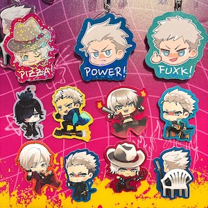 Könnte beinhalten: Eine Sammlung farbenfroher Schlüsselanhänger mit Anime-Charakteren. Jeder Schlüsselanhänger zeigt ein anderes Charakterdesign mit kräftigen Umrissen und leuchtenden Farben. Einige Schlüsselanhänger haben Text wie "PIZZA!" und "POWER!".