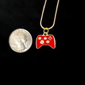 May include: A gold chain necklace with a red video game controller pendant. The controller has black buttons and a green and yellow accent.