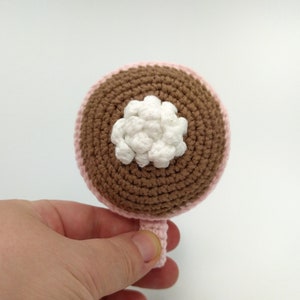 May include: A crocheted brown and pink cup with a white crocheted flower on top.