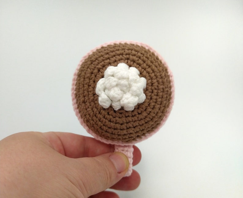 May include: A crocheted brown and pink cup with a white crocheted flower on top.