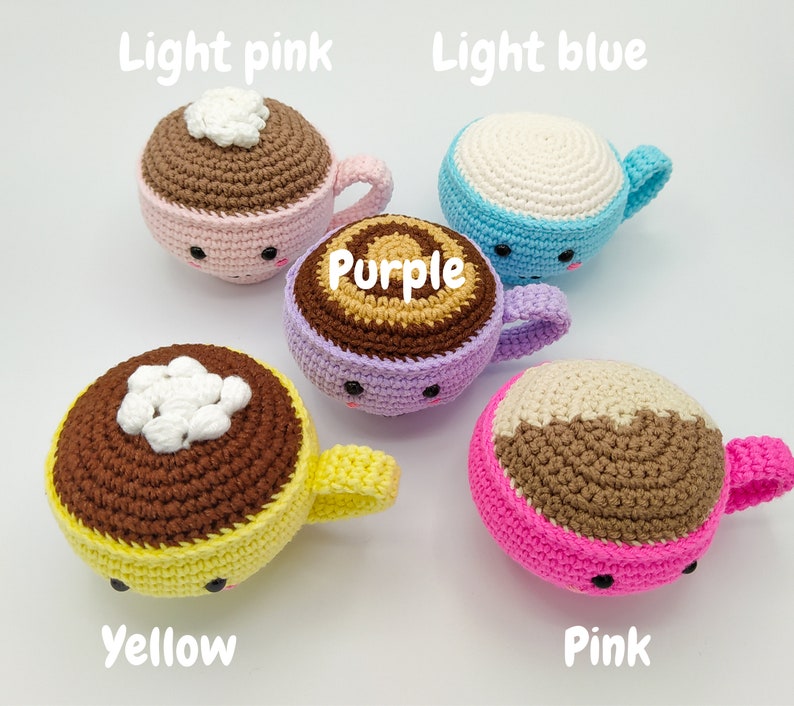 May include: Five crocheted coffee cup plushies in different colors. The cups are light pink, light blue, purple, yellow, and pink. Each cup has a brown crocheted rim and a white crocheted top. The cups have cute faces with black eyes and a small mouth.