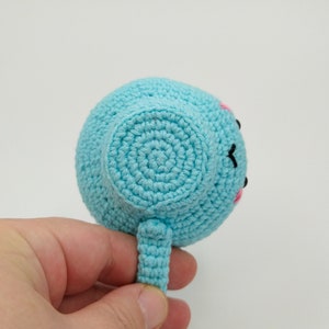 May include: A light blue crocheted stuffed toy shaped like a teacup with a pink and black face. The toy has a small handle.