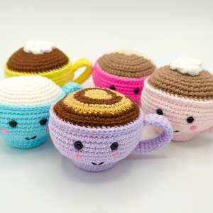 May include: Five crocheted coffee cup plushies in various colors, including blue, pink, purple, and yellow. Each cup has a cute face with eyes and a smile.