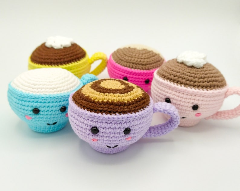 May include: Five crocheted coffee cup plushies in various colors, including blue, pink, purple, and yellow. Each cup has a cute face with eyes and a smile.