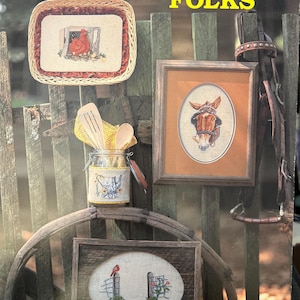 May include: A book cover titled "COUNTRY FOLKS" featuring cross-stitch designs. The cover displays framed cross-stitch art of a chicken, a horse, and a bird on a fence. A jar with wooden utensils and a decorative lid is also visible.