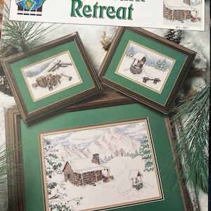 Pode incluir: Um kit de ponto cruz intitulado "Mountain Retreat" com cenas de paisagens de inverno emolduradas. O kit inclui três desenhos de ponto cruz emoldurados com cabanas cobertas de neve e fundos de montanhas. O kit é projetado por Gary Hanner.
