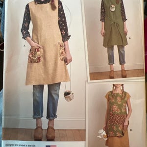 May include: Simplicity sewing pattern 8230 for Dottie Angel aprons in sizes XS-XL. The envelope displays three variations of sleeveless aprons with front pockets, shown in solid tan, solid olive green, and a floral green and yellow patchwork design.