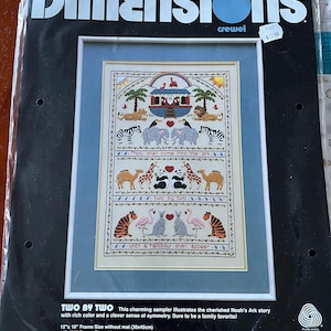 May include: A cross-stitch pattern featuring a colorful illustration of Noah's Ark with animals, surrounded by a blue frame. The text "Thou shall come into the ark... two by two... until a rainbow shall appear" is included. The pattern is 12 inches by 18 inches without a mat and 16 inches by 22 inches with a mat.