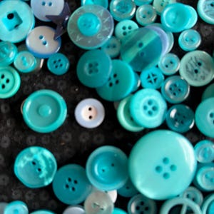 Könnte beinhalten: Eine Sammlung verschiedener türkisfarbener und blauer Knöpfe in unterschiedlichen Größen und Formen. Die Knöpfe, mit zwei oder vier Löchern, sind auf einer dunklen Oberfläche verstreut. Die Kollektion umfasst runde, quadratische und einzigartig geformte Knöpfe, ideal für Näh- und Bastelprojekte.