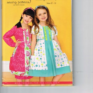 May include: A sewing pattern for a girl's dress called "Gretchen". The pattern is for a euro-style dress with oversized pockets and a square neckline. The pattern is available in sizes 2T-10. The image shows two girls wearing the dress, one in pink and one in blue and white.