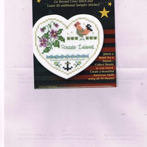 Puede incluir: Un patrón de punto de cruz para un sampler en forma de corazón que presenta un gallo, flores y un ancla. El patrón se titula "Rhode Island" y forma parte de la colección "Hearts of America". El patrón incluye instrucciones para aprender 50 puntos de bordado adicionales.