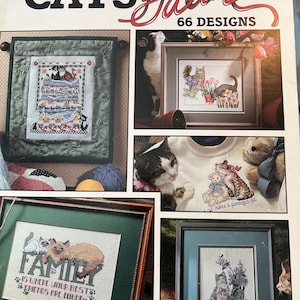 May include: A leaflet cover titled "CATS Galore" showcasing cross-stitch cat designs. The cover displays framed cross-stitch pieces with cats, a cat on a sweatshirt, and the text "FAMILY is where your best friends are found."