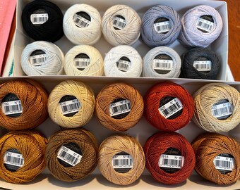 May include: A box of 18 spools of embroidery floss in various shades of brown, beige, and orange. The spools are labeled with the brand name "Anchor" and the number "8".
