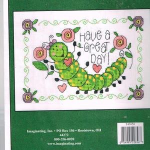 May include: Cross stitch pattern featuring a green caterpillar with yellow spots and pink hearts. The caterpillar is smiling and has a pink bow on its head. The text "Have a Great Day!" is written in pink letters above the caterpillar.