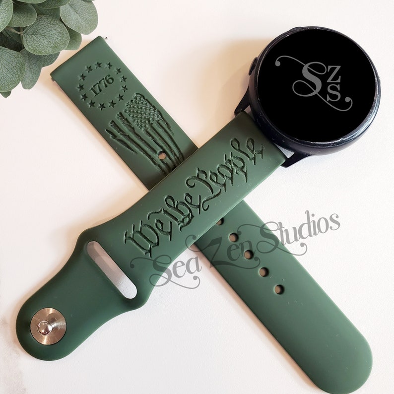 May include: Green silicone watch band with the text "We the People" and a star-shaped design with the number "1776" on one side. The other side of the band has a design of the American flag.