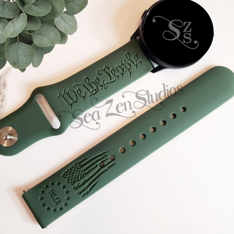 May include: A green silicone watch band with the text "We the People" engraved on one side and a stylized American flag with "1776" engraved on the other side.