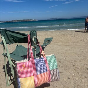 Puede incluir: Un bolso tote rectangular con un dise&ntilde;o de patchwork de cuadrados de tela de vichy en colores rojo, azul, verde, amarillo, naranja y marr&oacute;n. El bolso tiene dos asas de vichy rojo y el texto amarillo bordado "R BRIDE" en el panel frontal izquierdo.