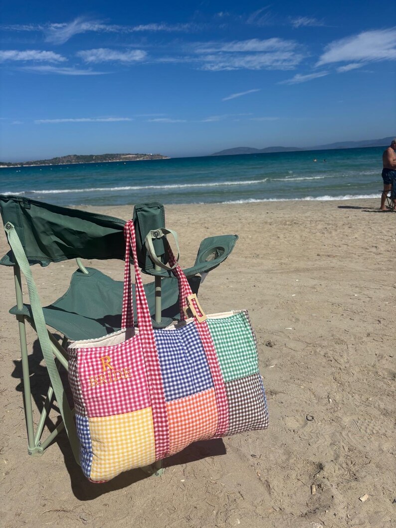 Puede incluir: Un bolso tote rectangular con un dise&ntilde;o de patchwork de cuadrados de tela de vichy en colores rojo, azul, verde, amarillo, naranja y marr&oacute;n. El bolso tiene dos asas de vichy rojo y el texto amarillo bordado "R BRIDE" en el panel frontal izquierdo.