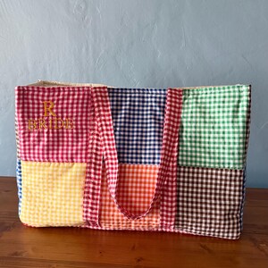 Puede incluir: Un bolso tote rectangular confeccionado con cuadrados de tela acolchada con un patr&oacute;n de cuadros vichy multicolor en rojo, amarillo, azul, naranja, verde y marr&oacute;n. La secci&oacute;n de cuadros rojos incluye el texto amarillo bordado R BRIDE.