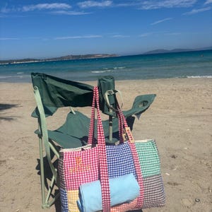 Puede incluir: Un bolso tote de patchwork con estampado de cuadros vichy en rojo y blanco y el texto bordado "BRIDE" en dorado. El bolso incluye paneles de cuadros vichy en amarillo, azul y verde, con asas de cuadros vichy rojo y blanco y una tela azul claro.