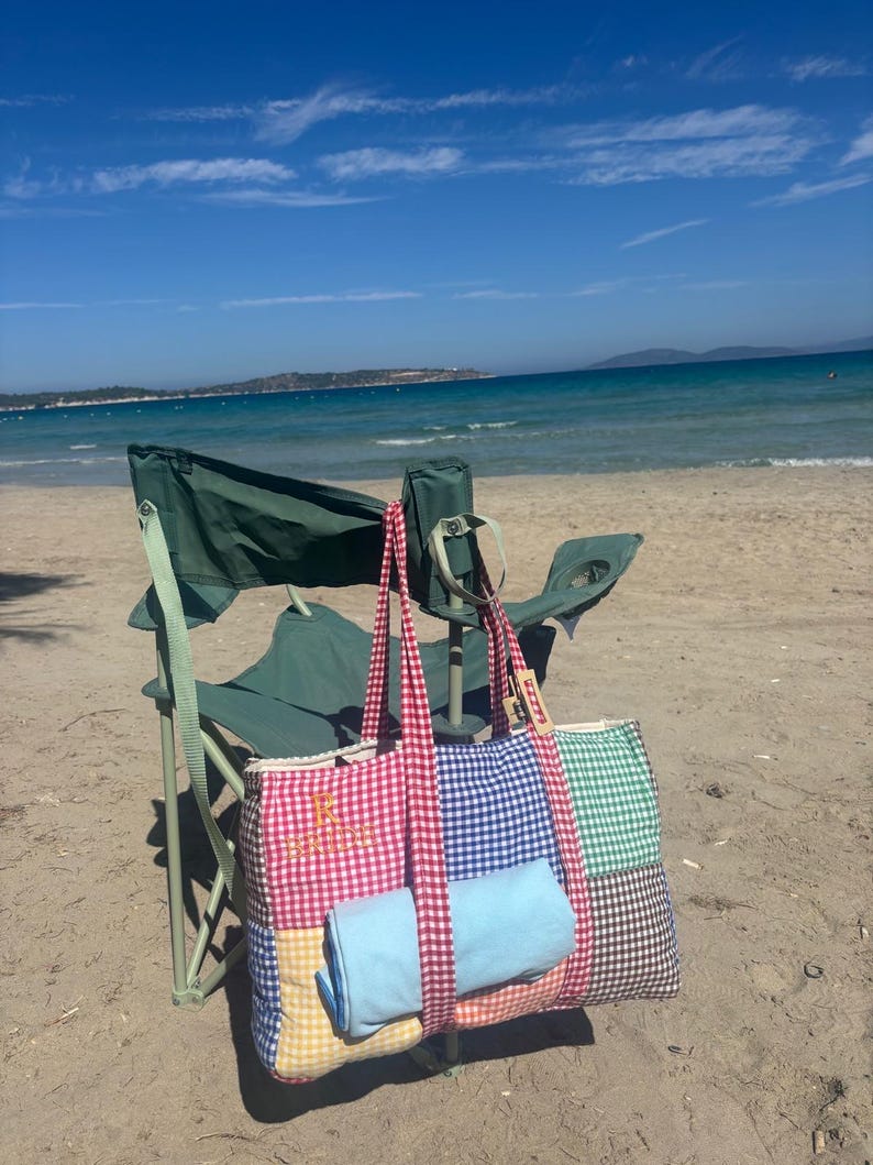 Puede incluir: Un bolso tote de patchwork con estampado de cuadros vichy en rojo y blanco y el texto bordado "BRIDE" en dorado. El bolso incluye paneles de cuadros vichy en amarillo, azul y verde, con asas de cuadros vichy rojo y blanco y una tela azul claro.