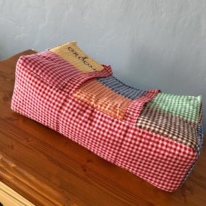 Puede incluir: Un organizador de tela rectangular con un dise&ntilde;o de patchwork de cuadros vichy en rojo, naranja, azul, verde y marr&oacute;n. La secci&oacute;n superior incluye un panel amarillo con la palabra GROOM impresa en negro. El art&iacute;culo tiene una textura acolchada.