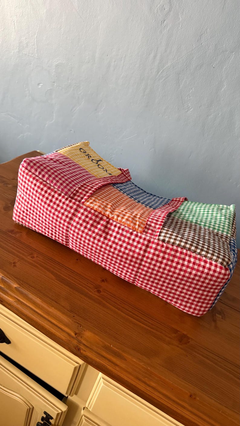 Puede incluir: Un organizador de tela rectangular con un dise&ntilde;o de patchwork de cuadros vichy en rojo, naranja, azul, verde y marr&oacute;n. La secci&oacute;n superior incluye un panel amarillo con la palabra GROOM impresa en negro. El art&iacute;culo tiene una textura acolchada.