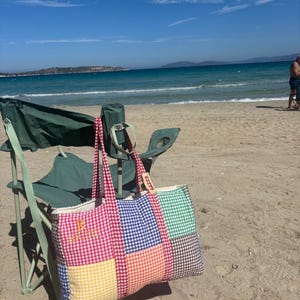 Puede incluir: Un bolso tote rectangular con un dise&ntilde;o de patchwork de cuadrados de tela de vichy en colores rojo, azul, verde, amarillo, naranja y marr&oacute;n. El bolso tiene dos asas de vichy rojo y el texto amarillo bordado "R BRIDE" en el panel frontal izquierdo.