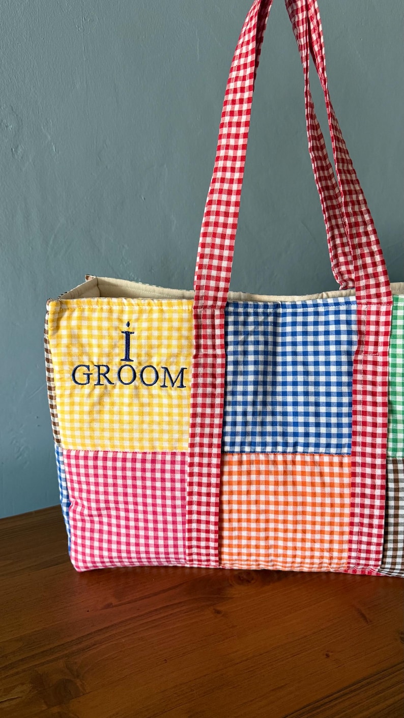 Puede incluir: Un bolso tote acolchado con un dise&ntilde;o de patchwork de cuadros vichy multicolores en amarillo, azul, rojo, naranja y verde. El bolso tiene asas de cuadros vichy rojos y blancos y el texto azul oscuro bordado I GROOM en el cuadrado amarillo.