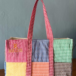 Puede incluir: Un bolso tote rectangular con un patr&oacute;n de patchwork de cuadros vichy multicolor en rojo, azul, verde, amarillo, naranja y marr&oacute;n. El bolso tiene dos asas de cuadros vichy rojos y blancos y el texto bordado en amarillo R BRIDE en el frente.