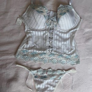 May include: White and light blue striped lingerie set. The set includes a bustier with a lace trim and a matching thong. The bustier has a lace-up front and adjustable straps. The thong has delicate ties on each side.