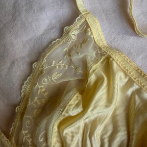 May include: A pale yellow bra with delicate lace detailing. The bra features a soft, silky fabric with a subtle sheen. The straps and edges are trimmed with a matching yellow color, creating a cohesive and elegant design.