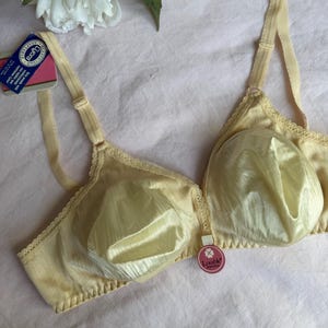 May include: A pale yellow bra with adjustable straps and a delicate lace trim. The bra has a textured fabric and a tag that reads "Lycra Adaptable". The bra is displayed on a pink surface.