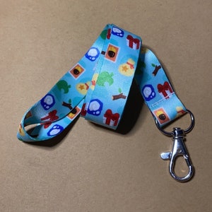 May include: A blue lanyard with a repeating pattern of Animal Crossing characters and items. The lanyard has a silver swivel clip.