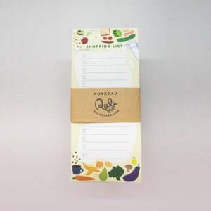 Op de afbeelding: Een notitieblok met een gele achtergrond en een kleurrijke illustratie van voedsel rond de rand. Het notitieblok heeft een bruin papieren label met de tekst "NOTEPAD" en "lala crafts" met het websiteadres "balaclara.com". Het notitieblok heeft een sectie bovenaan met de tekst "SHOPPING LIST" met een checklist.