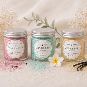 Peut inclure: Trois pots en verre avec des couvercles argentés remplis de sels de bain colorés. Les pots sont étiquetés "SELS DE BAIN NATURELS". Les pots mesurent environ 5 cm de haut et 5 cm de large. Sels roses, bleus et jaunes visibles. Fleurs et gousses de vanille.