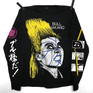 May include: Black long-sleeve shirt with a graphic of Bull Nakano, featuring yellow hair and blue facial markings. The shirt displays the text "BULL NAKANO" and Japanese text. A small logo is on the left sleeve.