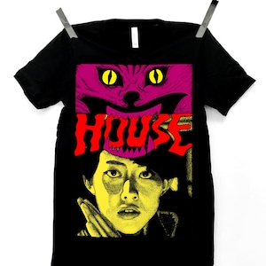May include: Black t-shirt featuring a graphic design with a purple cat face with yellow eyes above the red word "HOUSE". Below the word is a yellow and black illustration of a person.