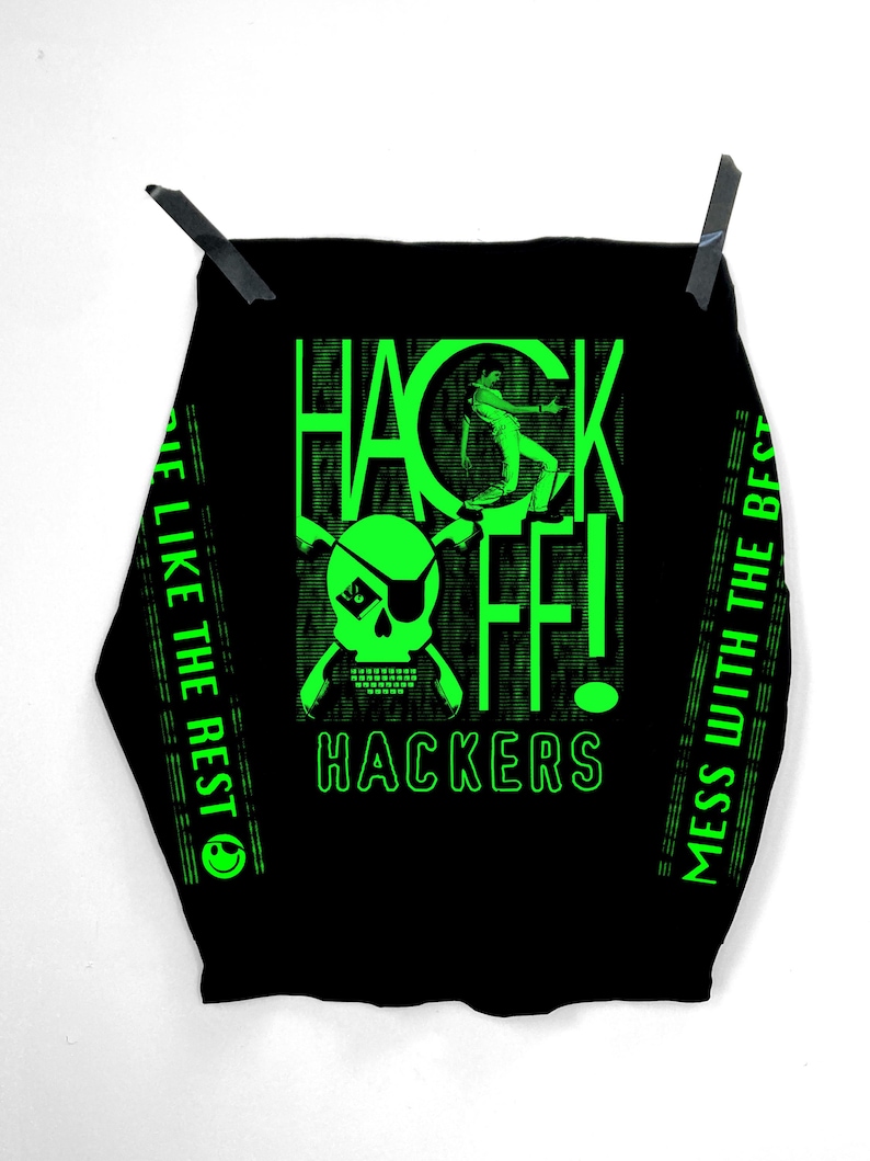 Op de afbeelding: Zwart T-shirt met een groen grafisch ontwerp dat "Hack Off!" zegt met een schedel en gekruiste beenderen en de tekst "Hackers". De tekst "Mess with the best..." en "...be like the rest" staat aan de zijkanten van het shirt.