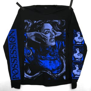 May include: A black long-sleeve shirt featuring a blue graphic print of a person with a distressed expression surrounded by tentacles. The left sleeve displays the text POSSESSION, while the right sleeve features three stacked images of a figure with a snake and the words Inhuman, ecstasy, and fulfill.