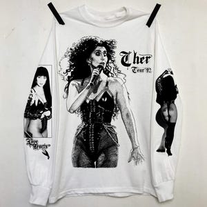 Peut inclure: T-shirt à manches longues blanche avec une image en noir et blanc de Cher sur le devant. L'image comprend le texte "Cher Tour '92".