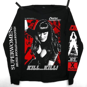 Peut inclure: T-shirt noir à manches longues avec un graphisme de femme et le texte "KILL...KILL!". Le t-shirt comporte également le texte "SUPERWOMEN. BELTED, BUCKLED and BOOTED!" et "Faster, PUSSYCAT!" en blanc.