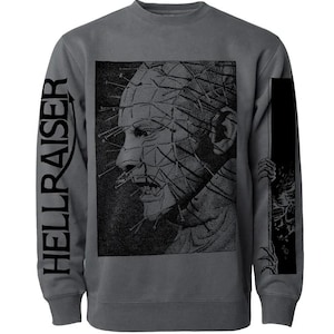 May include: Dark gray sweatshirt featuring a black and white graphic of a character with pins in their head. The word "HELLRAISER" is printed vertically on the left sleeve. A horror-themed design.