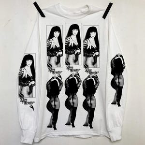 Peut inclure: T-shirt blanc à manches longues avec une image en noir et blanc d'une femme en tenue révélatrice. Le t-shirt comporte plusieurs images de la femme, avec le texte "Love Hurts" imprimé.