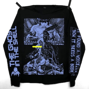 May include: Black long-sleeved top with a graphic from "The Ghost in the Shell." The design features detailed character illustrations and the text "THE GHOST IN THE SHELL" and "FOUND A VOICE, NOW IT NEEDS A BODY."