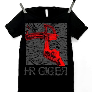 May include: Black t-shirt with a red and grey graphic design and the text "HR GIGER". The design features an abstract, stylized image. The t-shirt is suspended from a clothesline.
