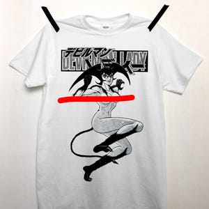 May include: White t-shirt featuring a black and white illustration of a female demon with horns and a tail. The shirt has the Japanese text "Devilman Lady" in a black rectangular box above the illustration.